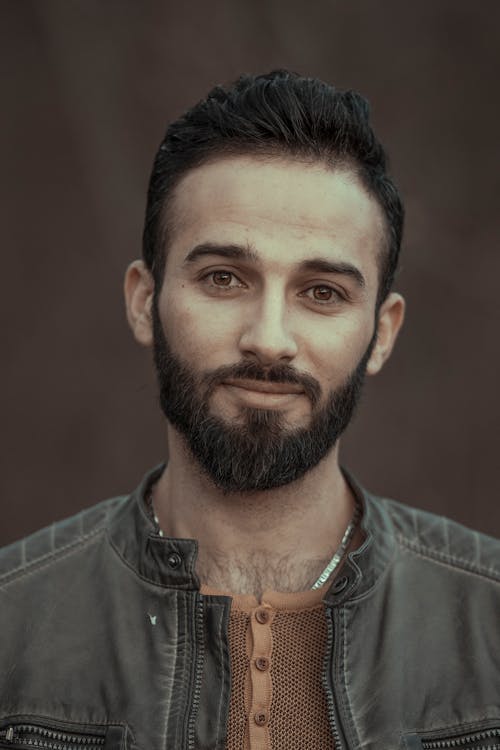 Free Masculine male with beard wearing jacket smiling while looking at camera against blurred background Stock Photo