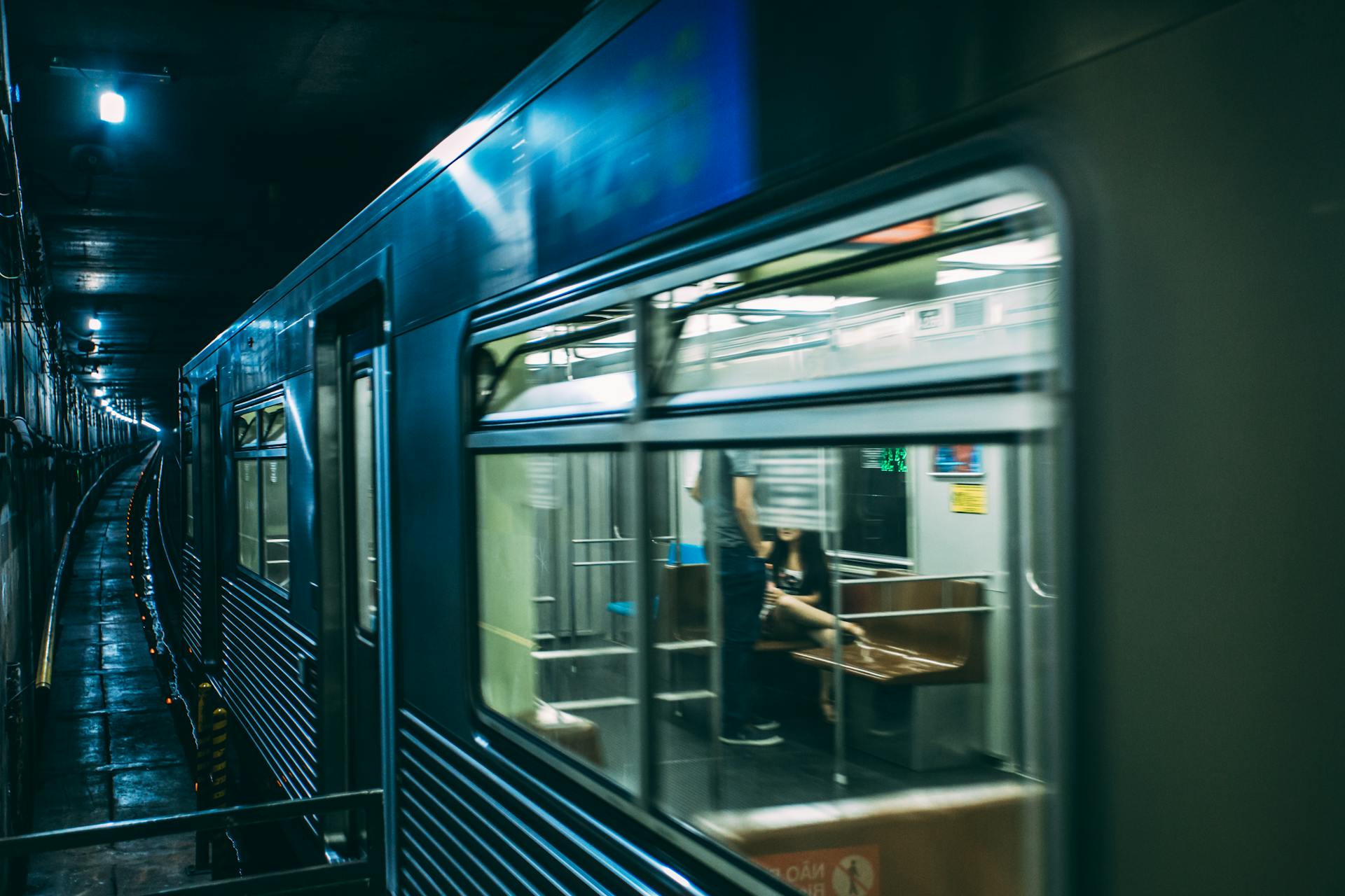 A subway train in motion with visible passengers in an urban underground setting.