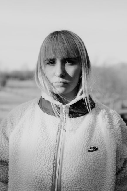 Grayscale portrait of a woman with bangs in a cozy jacket outdoors, exuding a 90s street fashion vibe.