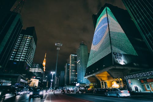 Cars Traveling on Road Between Buildings during Nighttime