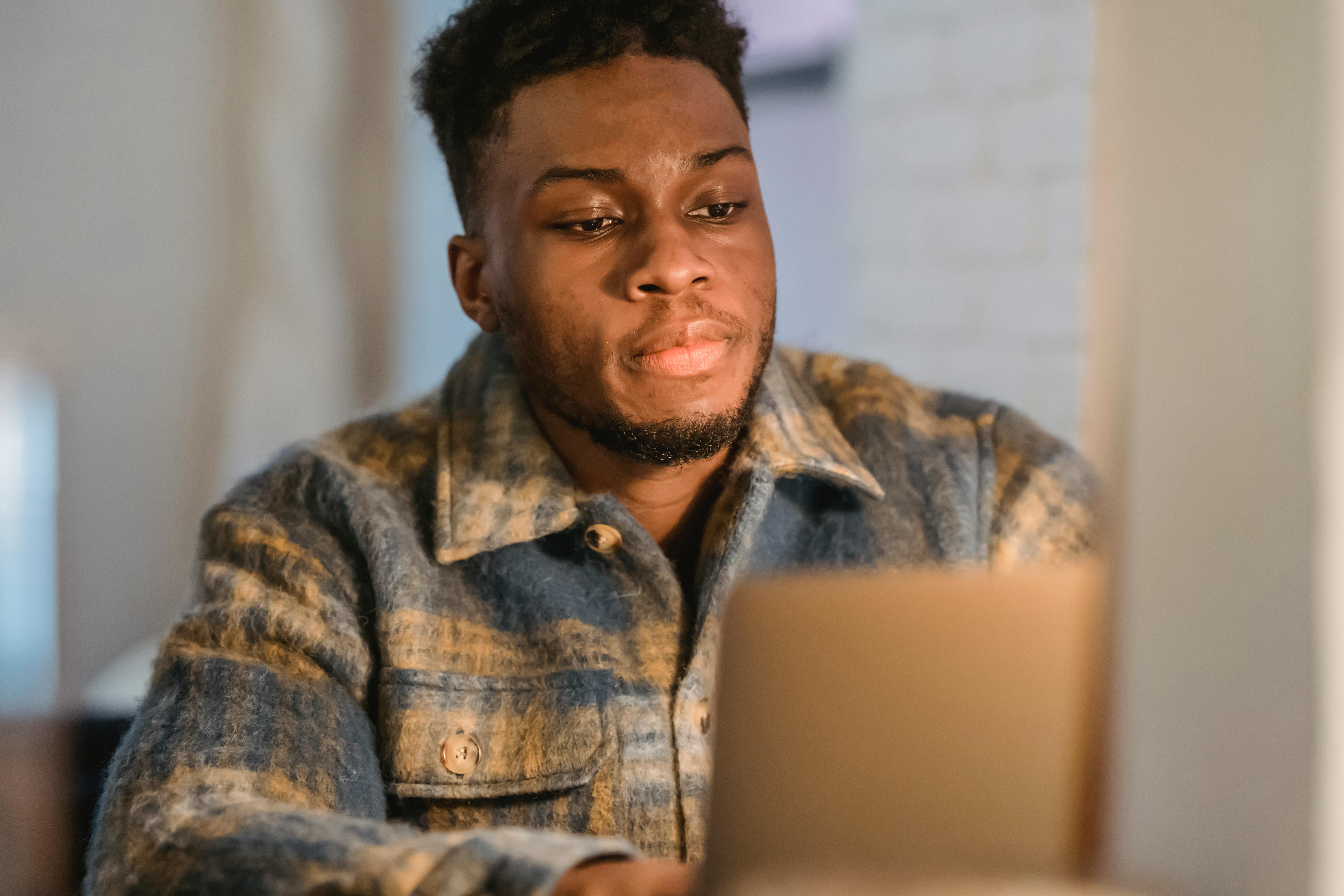 thoughtful black guy browsing laptop in room