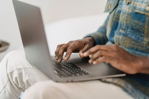 Free Crop faceless black male freelancer sitting on comfortable couch and typing on laptop keyboard while working remotely from home Stock Photo