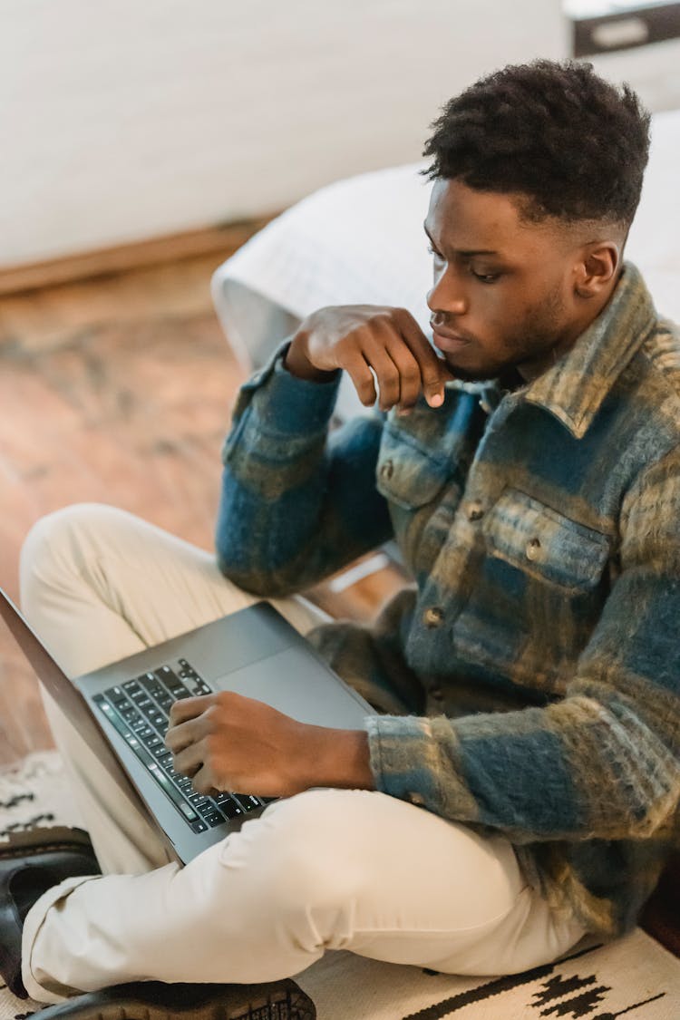 Serious African American Male Freelancer Using Laptop Sitting On Floor At Home