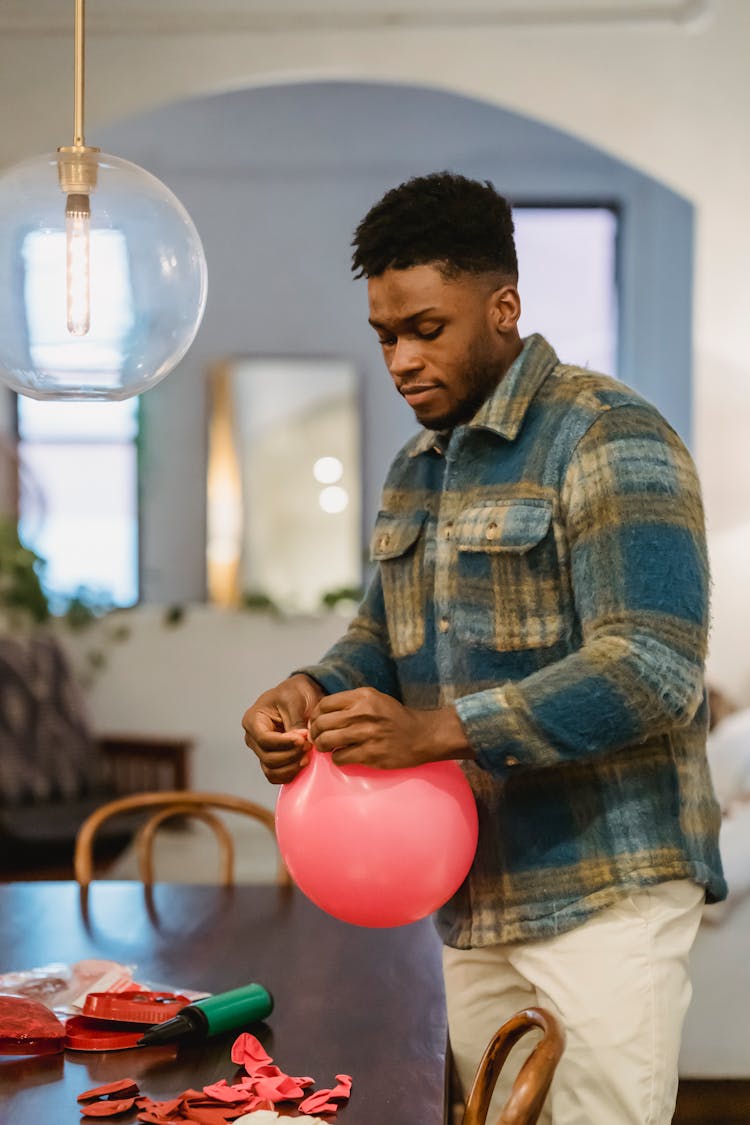 Young Black Man Tying Knot On Balloon During Party Preparation At Home