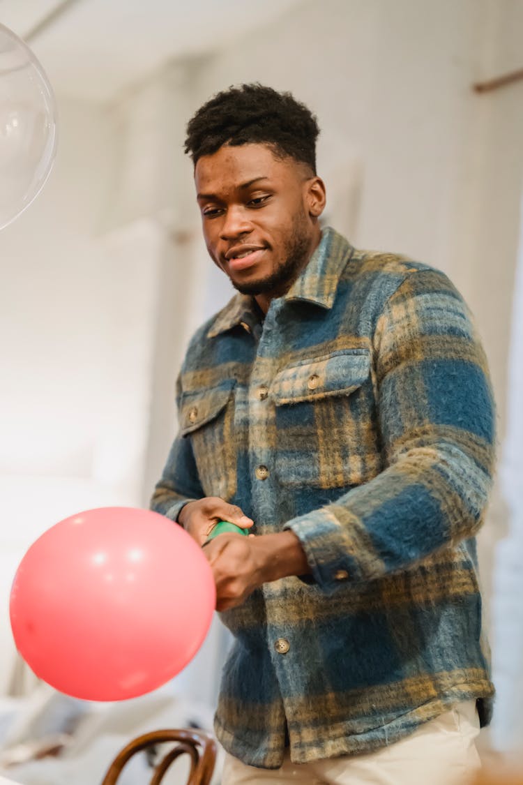 Happy Young Black Man Blowing Balloon With Pump At Home