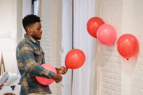 Free Side view of stylish young black male with Afro hair in casual outfit decorating apartment with red and pink balloons on Saint Valentines Day Stock Photo