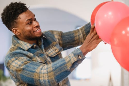 Bearded black man in checkered shirt correcting red balloons position while decorating room to special event