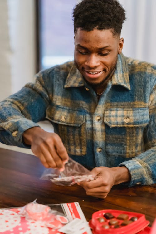 Young bearded African American male sitting at table with bag of decorations to Saint Valentine Day while preparing special holiday