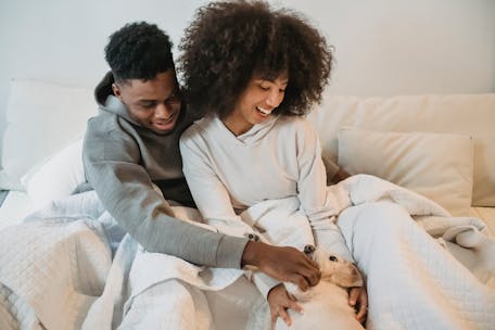 A cheerful couple enjoys a cozy morning in bed with their pet dog, embodying warmth and affection.