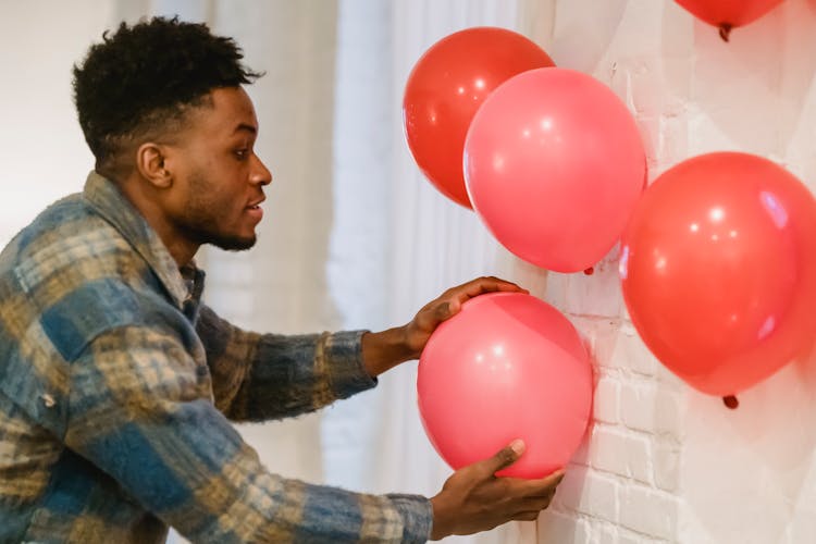 Young Black Man Placing Balloons On Wall