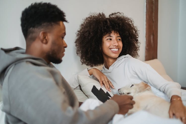 Happy Black Couple Resting On Couch With Obedient Dog