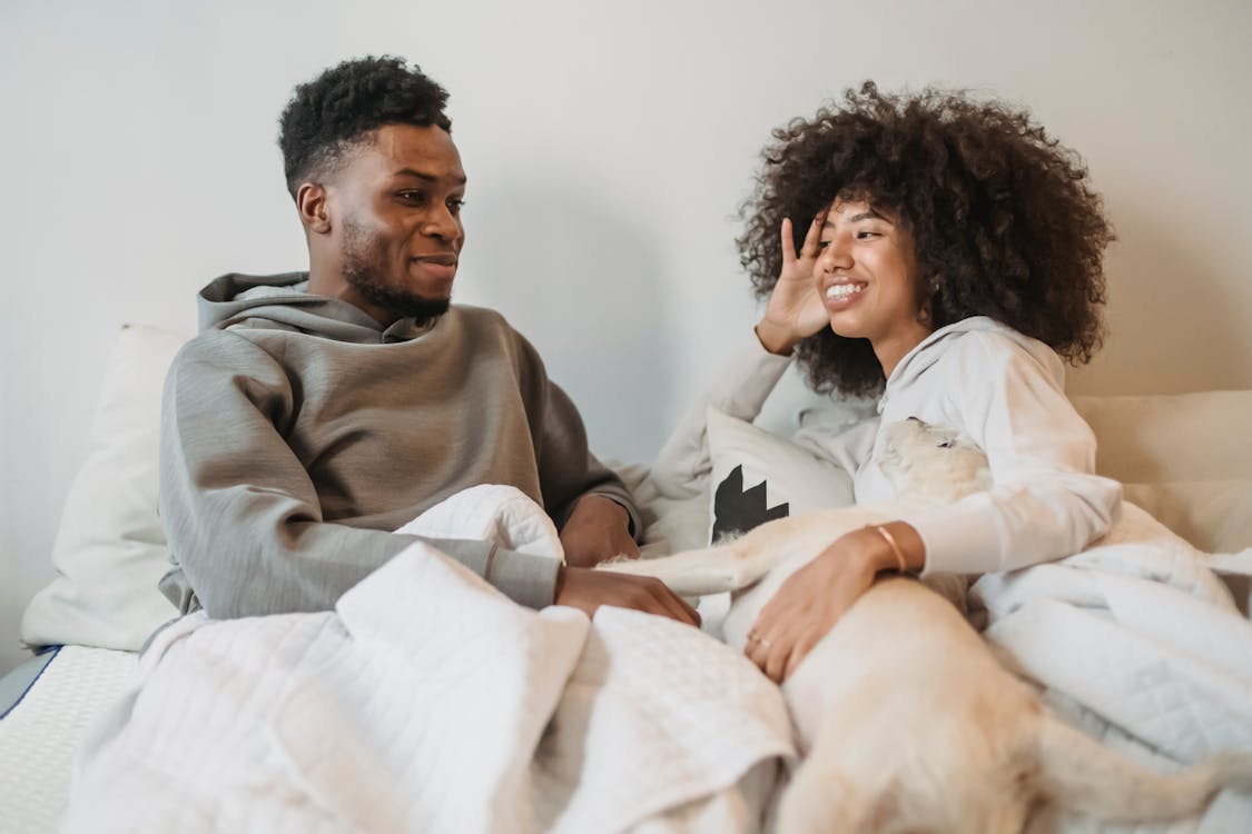 Free Positive young black couple talking while resting on bed and caressing dog Stock Photo