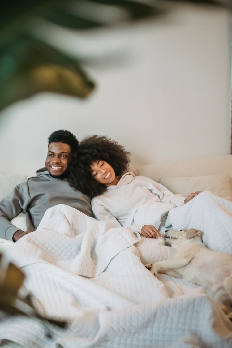 Delighted Young African American Couple Cuddling On Bed Near Sleeping Dog