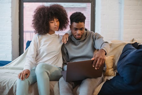 Black couple sitting on sofa and looking at laptop