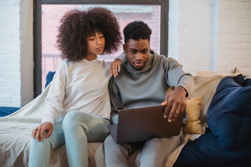 Free African American couple in casual clothes sitting on comfortable sofa at home and browsing netbook in daytime Stock Photo