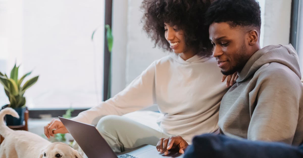 Cheerful black couple browsing laptop while spending time at home with dog