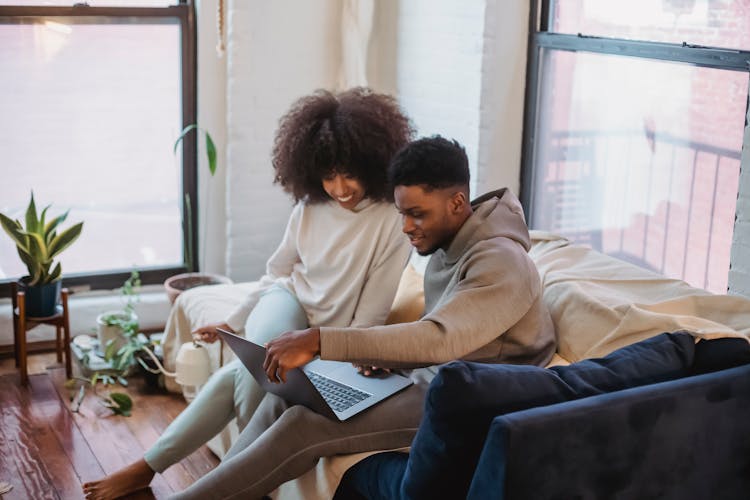 Cheerful Black Couple Browsing Laptop In Light Living Room In Daytime