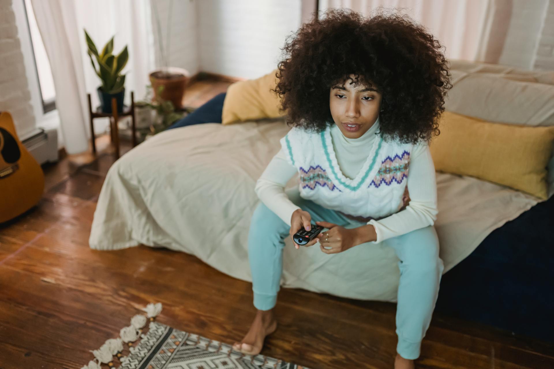 From above of concentrated young African American female with dark curly hair in casual outfit watching TV with interest while resting on sofa at home