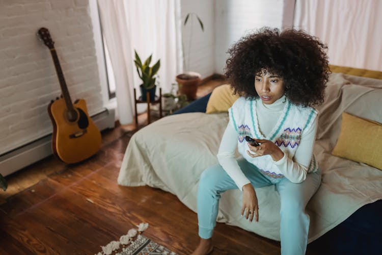 Calm Young Ethnic Woman Watching TV Sitting On Couch During Weekend At Home