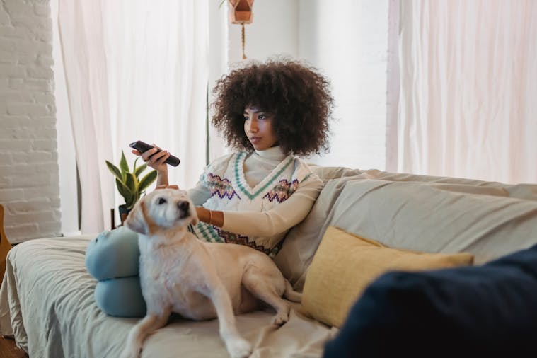 Young woman with curly hair relaxing with her dog on the sofa while watching TV.