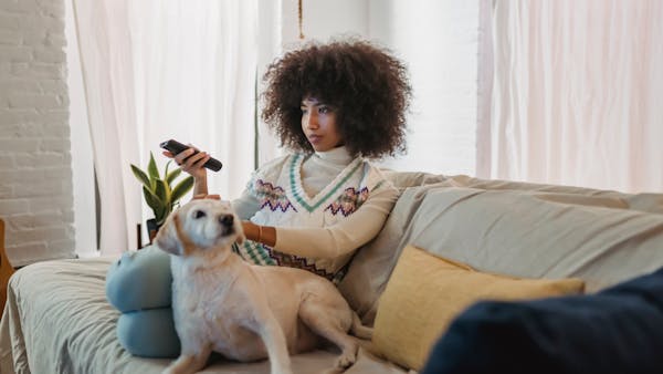 Young woman with curly hair relaxing with her dog on the sofa while watching TV.
