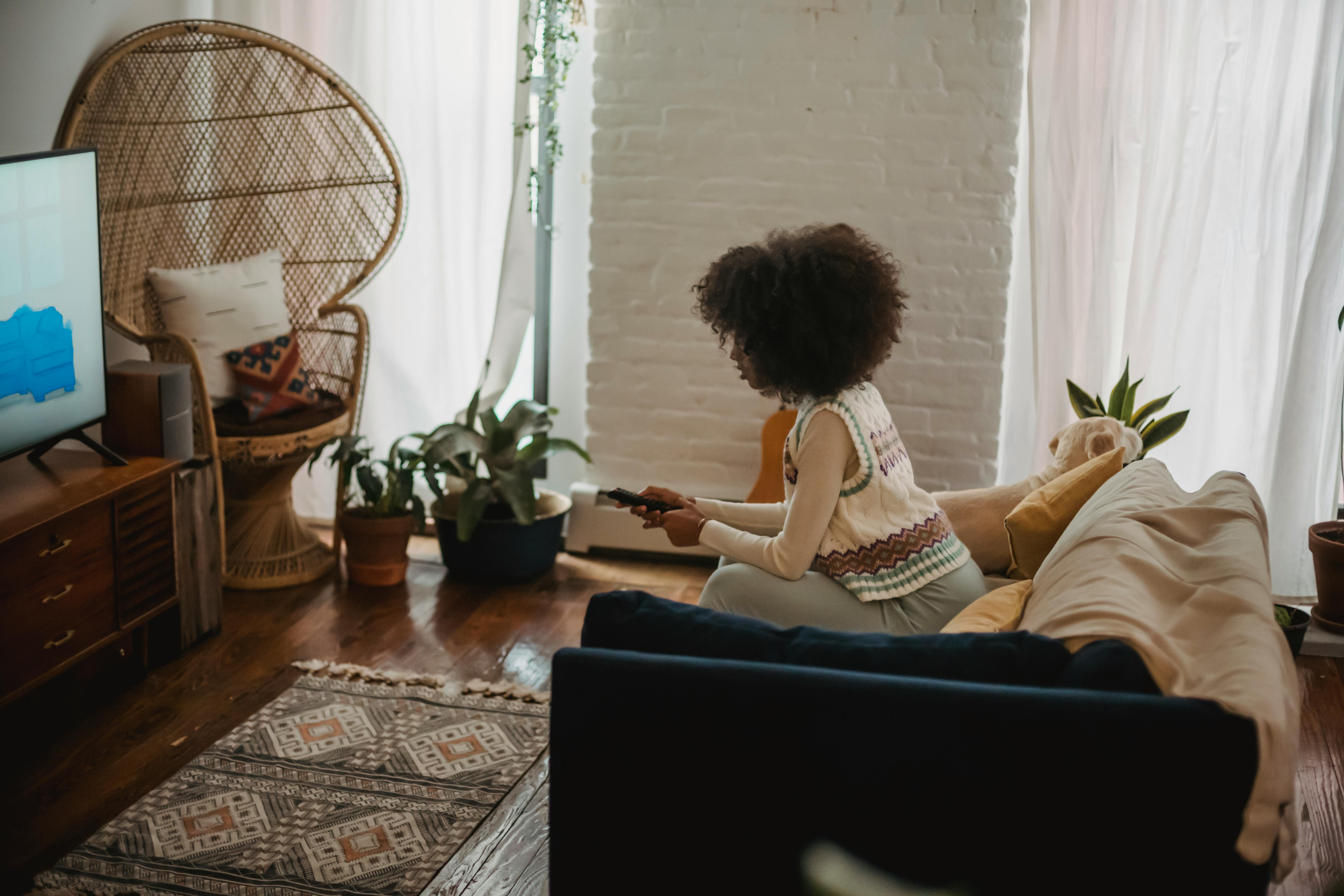 focused young ethnic woman with remote controller watching tv at home