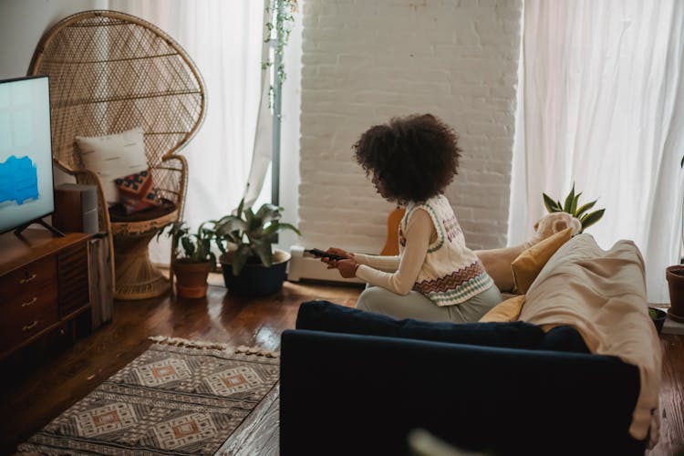 Focused Young Ethnic Woman With Remote Controller Watching TV At Home