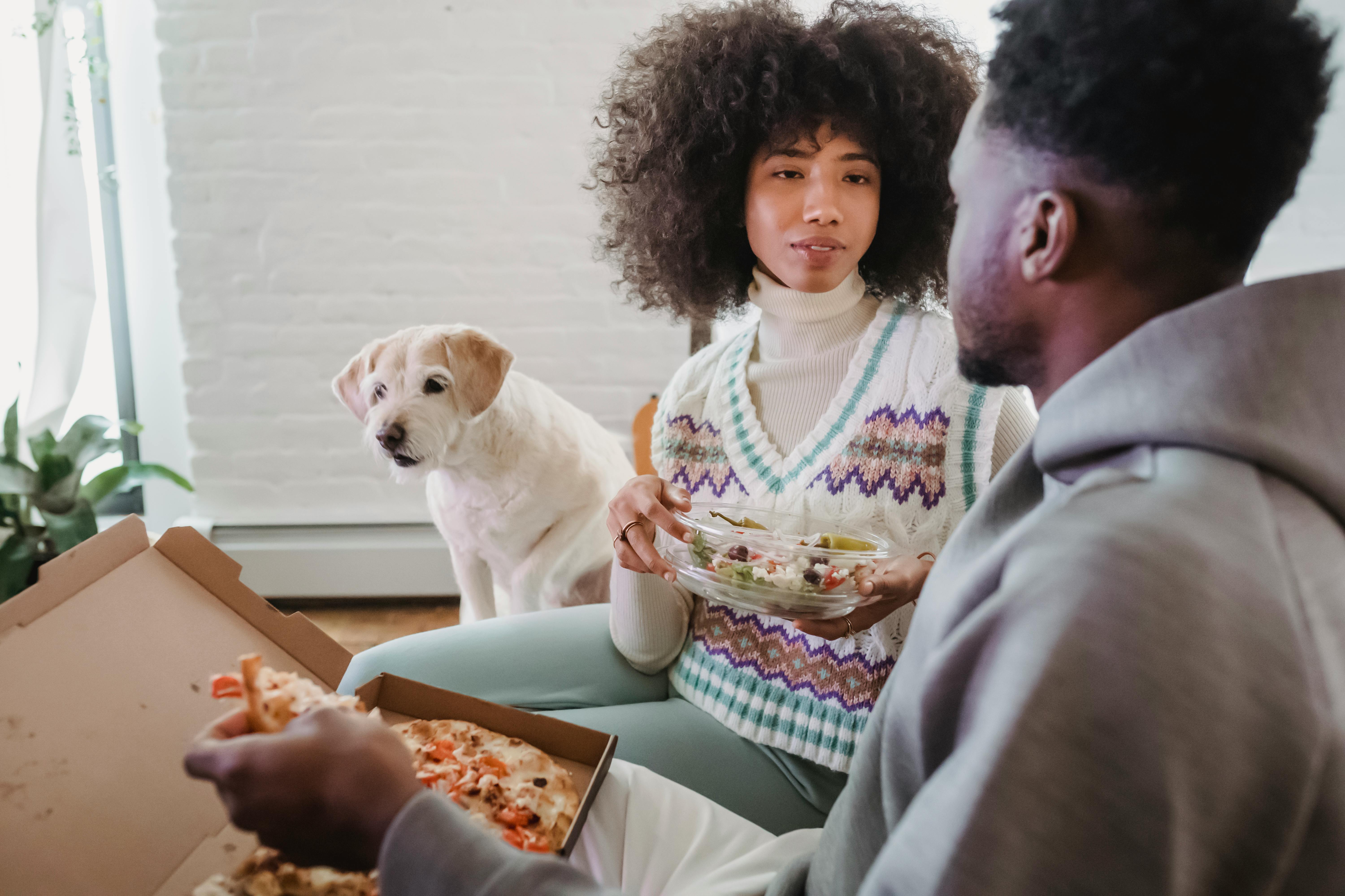 black couple talking while eating pizza and salad near dog