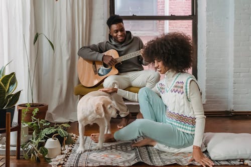 Black girlfriend entertaining with dog while boyfriend playing guitar