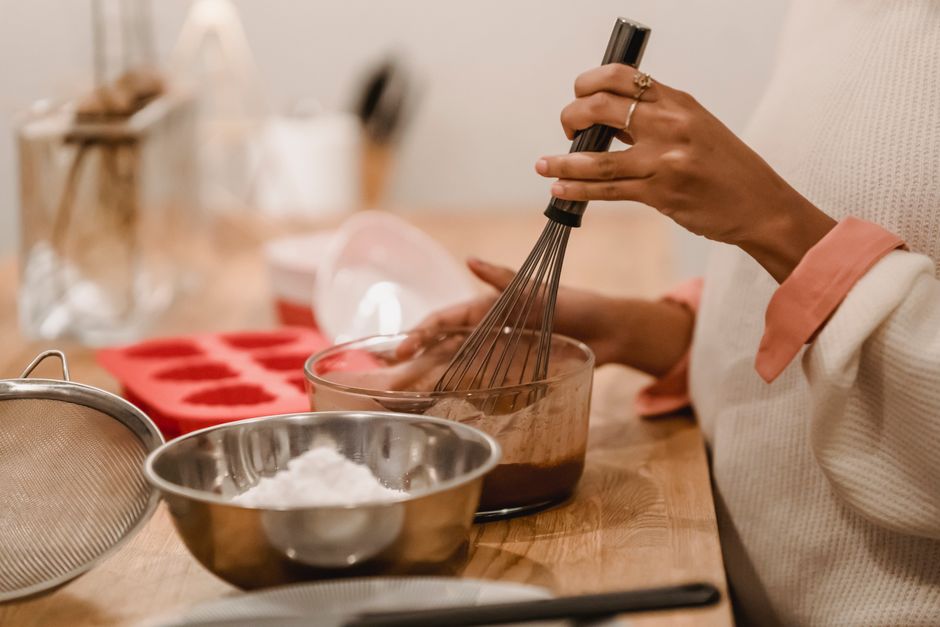 Side view of crop anonymous African American female whisking melted chocolate near metal bowl with flour in kitchen