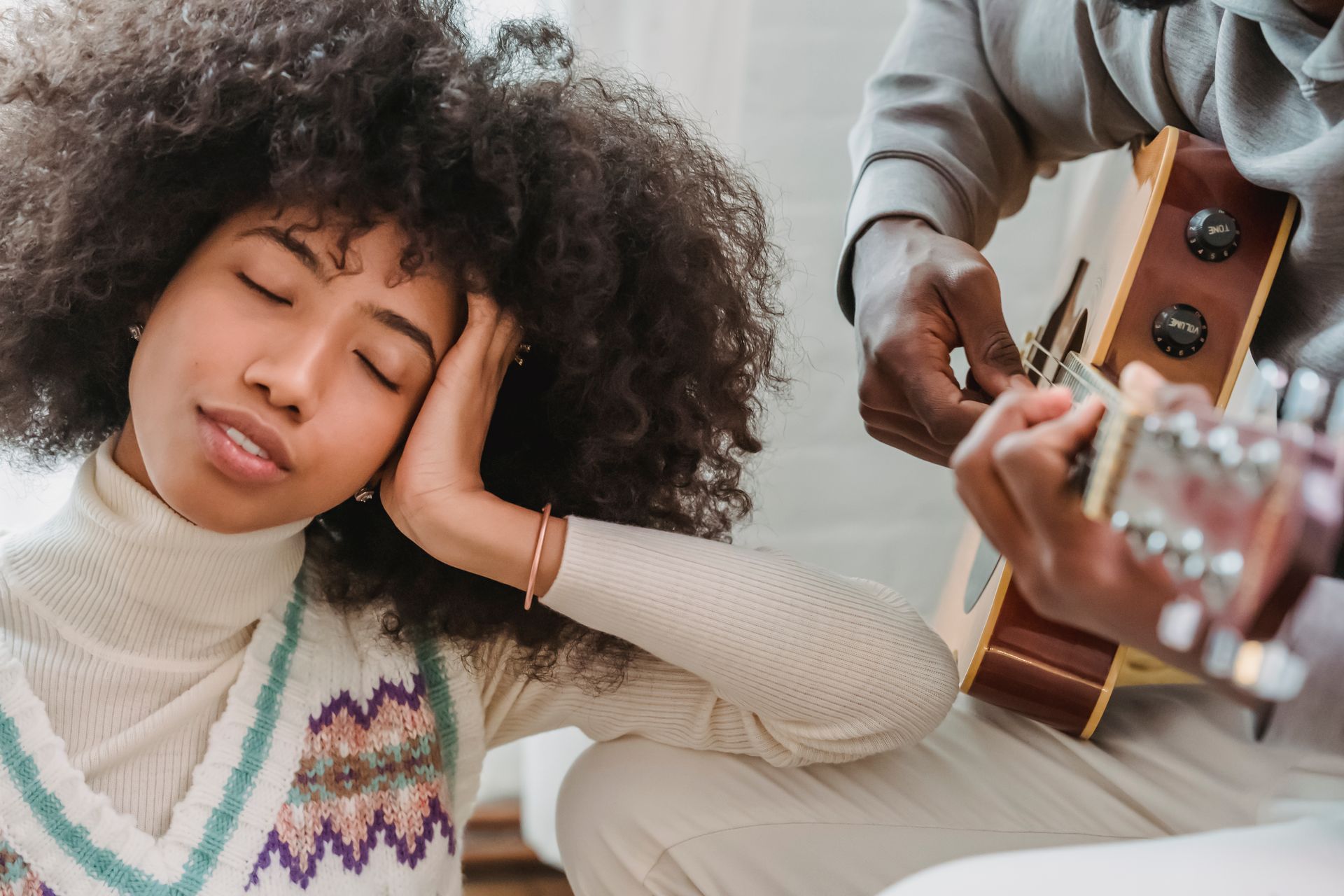 Satisfied African American female with closed eyes listening to anonymous black boyfriend playing song on acoustic guitar while spending time together