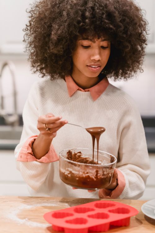 Free Concentrated African American female adding chocolate batter from bowl into silicone molds at table while cooking in kitchen on blurred background Stock Photo