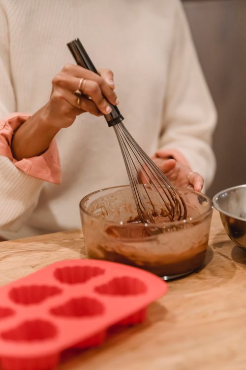 Free Unrecognizable female cook with whisk mixing batter in bowl while standing at table with silicone mold during cooking in kitchen Stock Photo