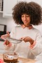 Content African American female cook pouring flour from sieve into bowl with batter while preparing delicious dessert in kitchen at table