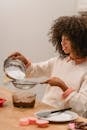 Side view of focused African American female sifting flour into bowl with batter while preparing pastry in kitchen at table