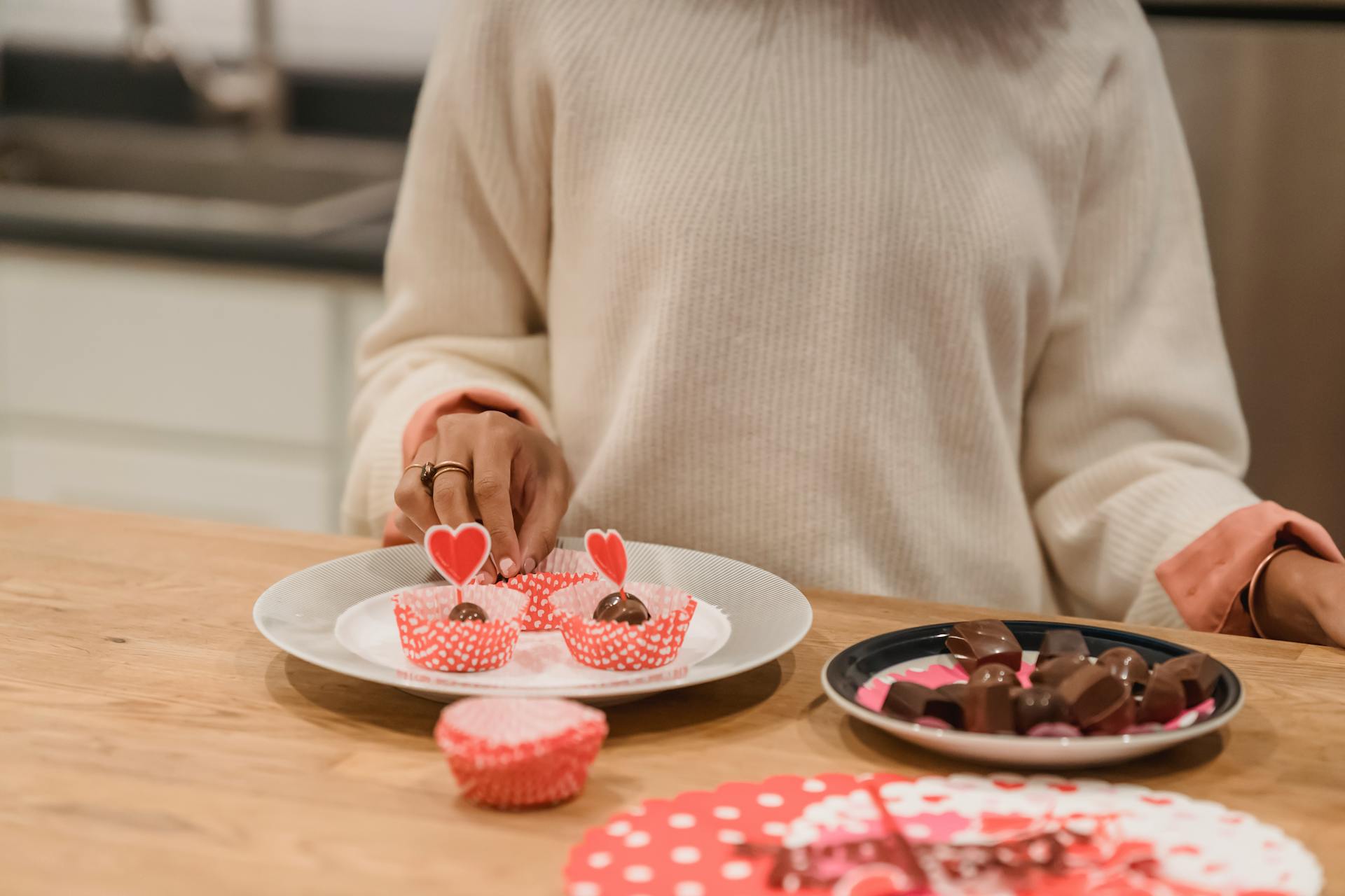 Unrecognizable female standing at wooden table with plates of delicious sweet chocolate candies served in molds in kitchen at home