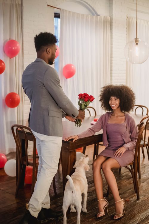 Free Happy black female looking at bouquet while unrecognizable boyfriend giving flowers in festive atmosphere Stock Photo