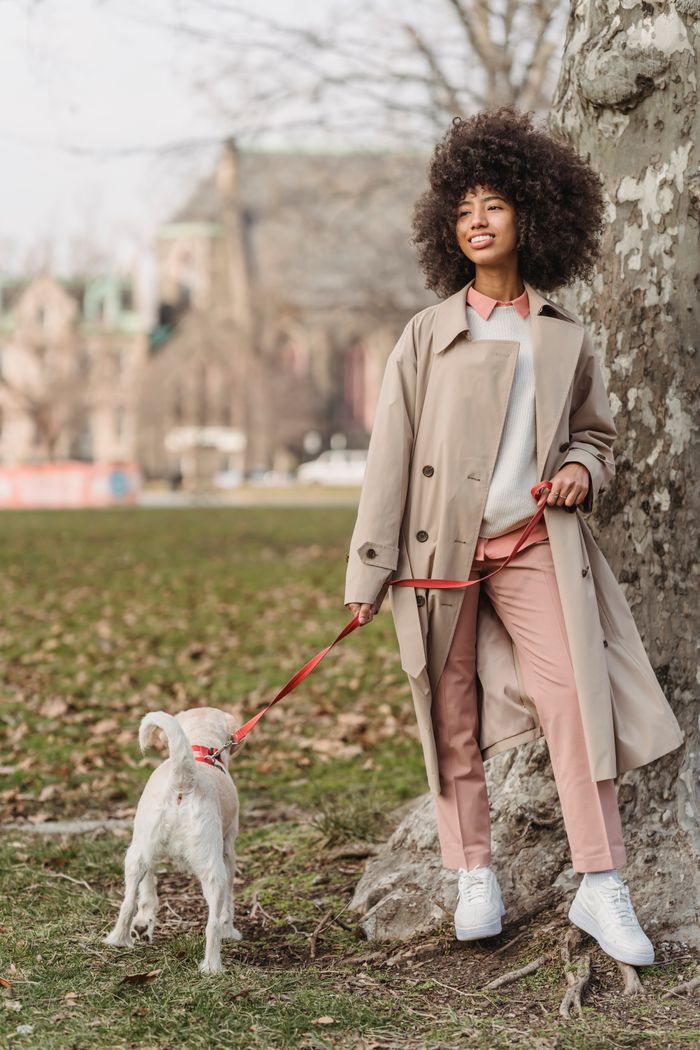 Cheerful woman walking a little white dog on a leash in the park