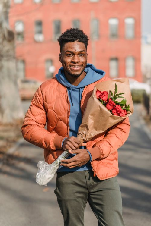 Free Happy African American male with fresh red roses in paper package on blurred background of town Stock Photo