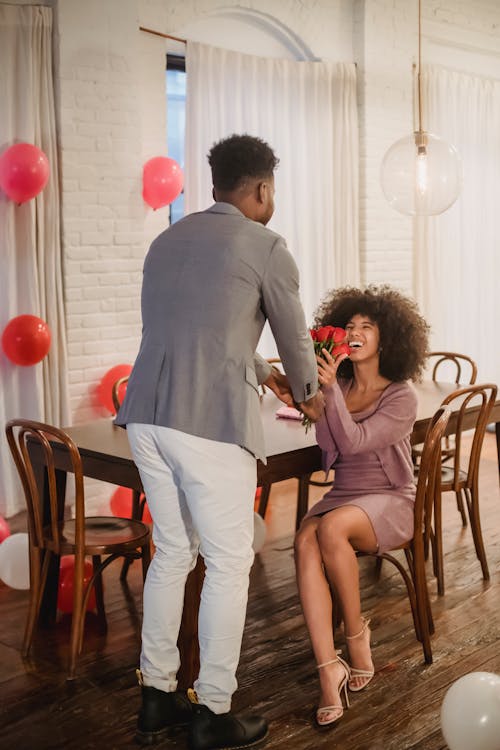 Free Black man giving bouquet of roses to woman at table Stock Photo