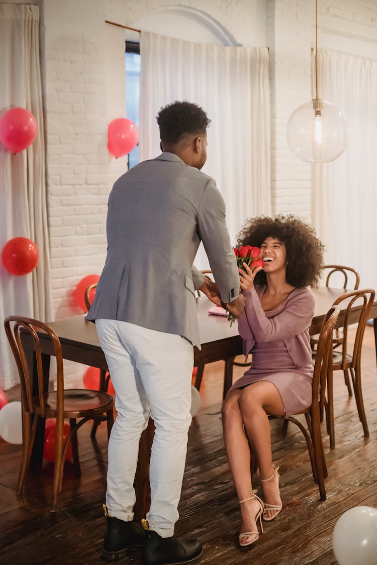 Black Man Giving Bouquet Of Roses To Woman At Table