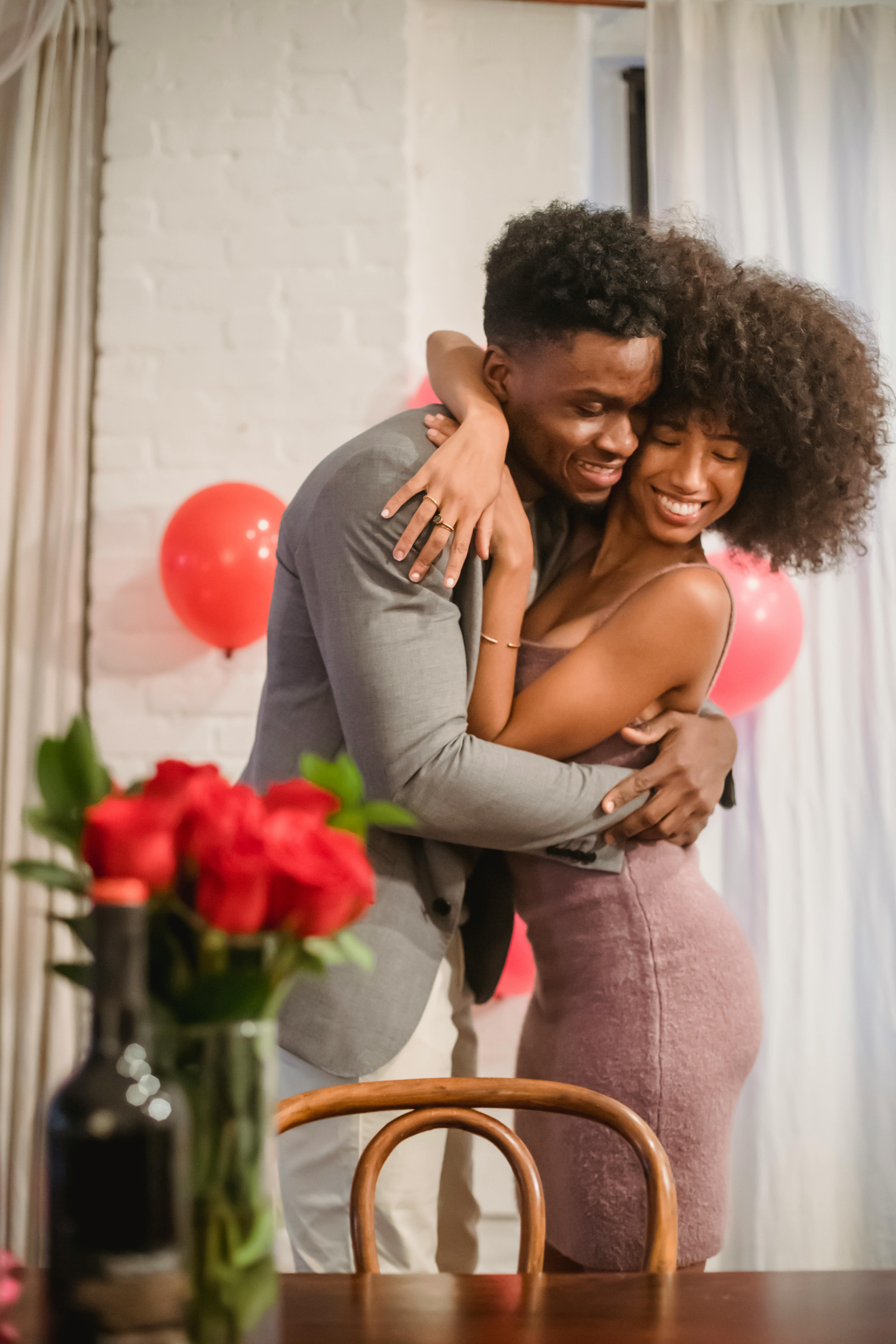 happy black couple hugging in loft near table with flowers