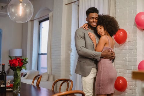 African American couple hugging and dancing near table in apartment