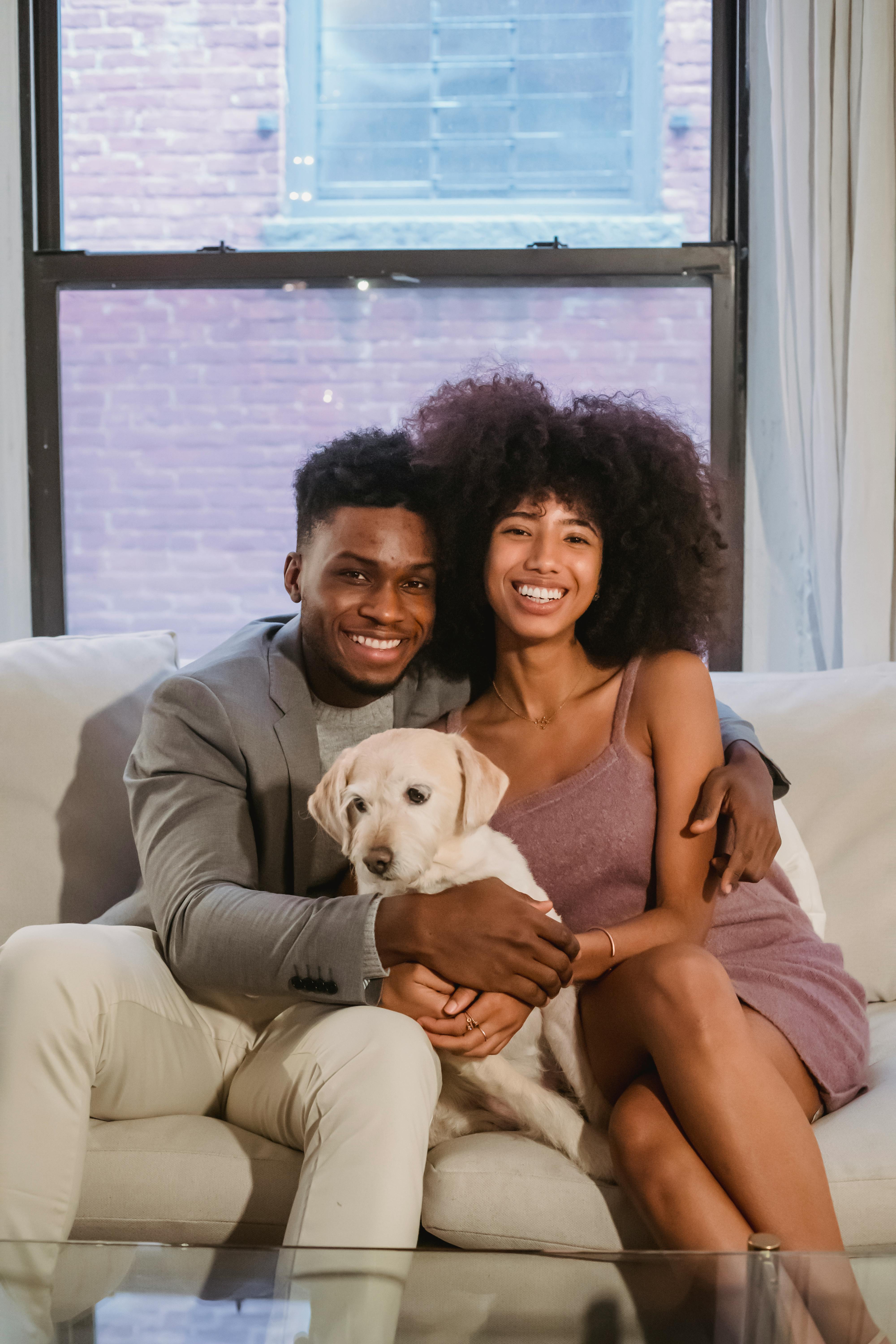 loving young african american couple cuddling while sitting on sofa with cute dog