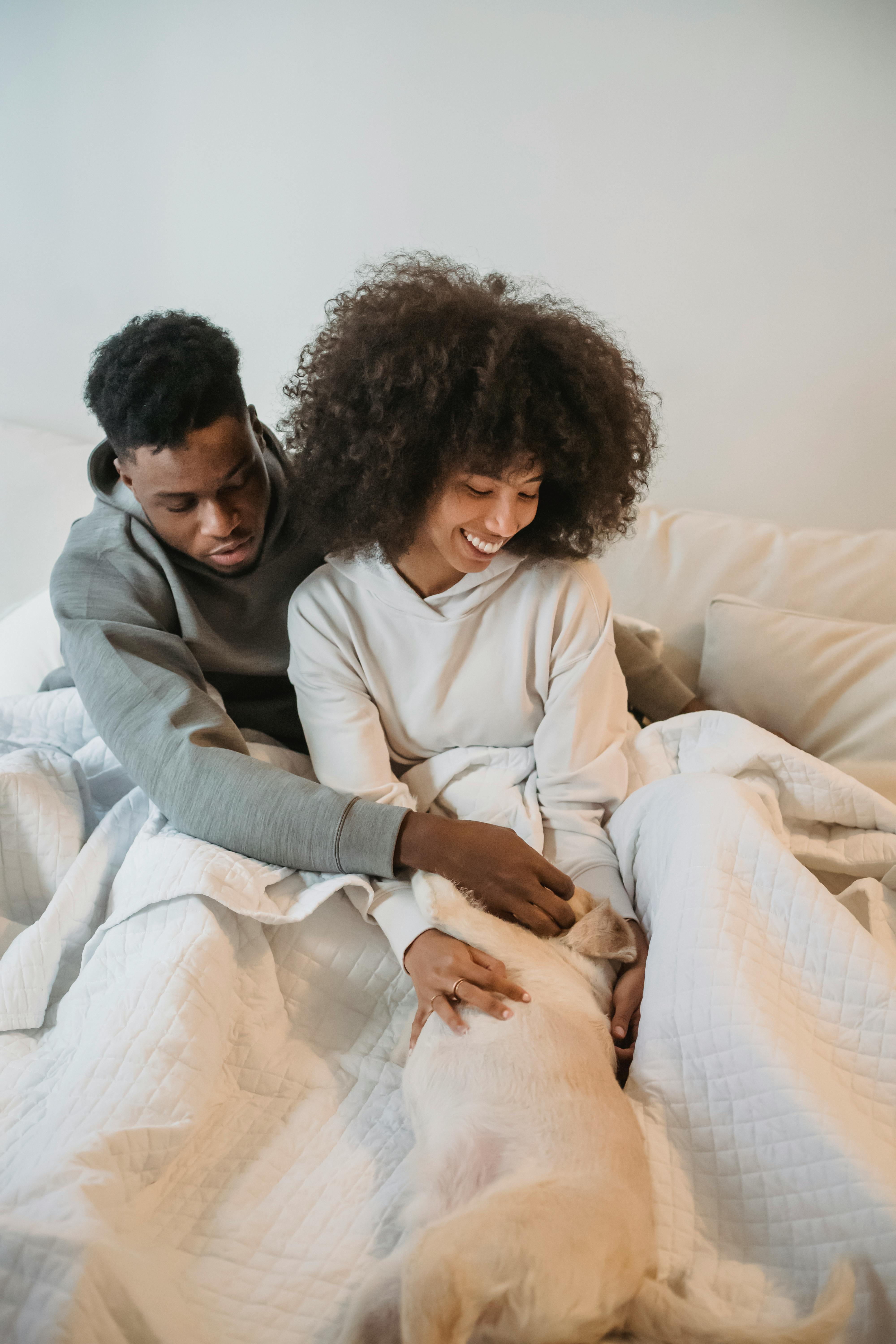 Positive young black couple stroking dog in bed