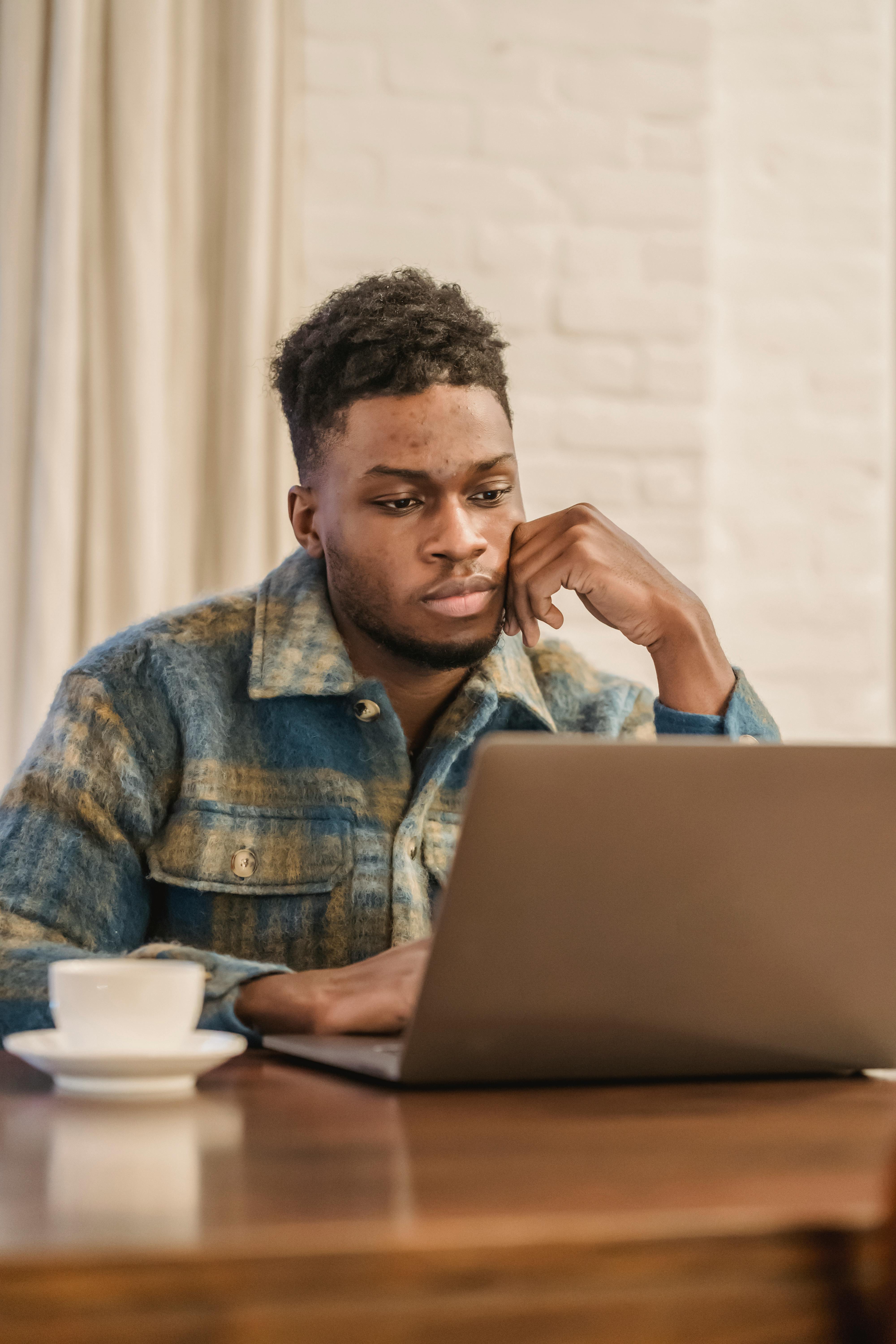 concentrated young black guy sitting at table and working remotely on netbook