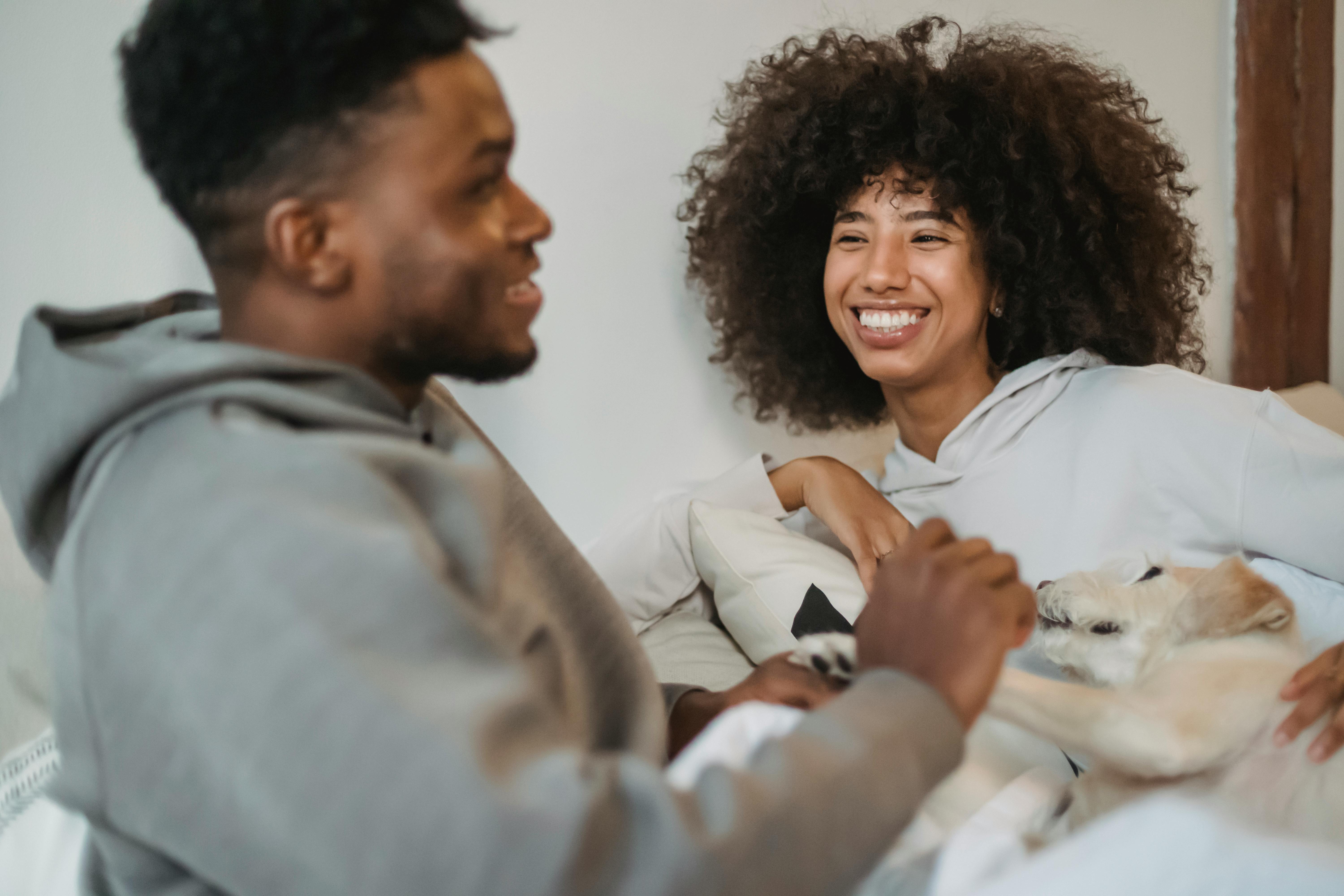 positive black couple resting in bed with dog and chatting