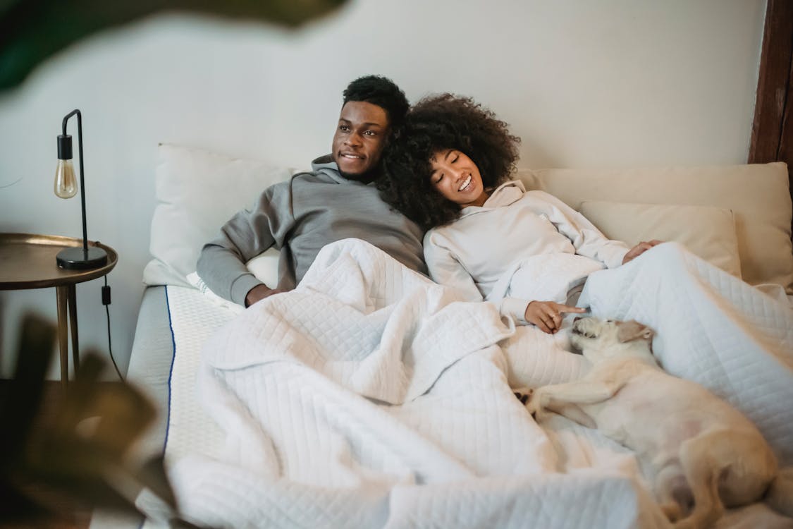 Free Happy ethnic couple lying in bed with dog during lazy weekend at home Stock Photo