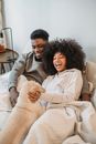 From above of happy young African American couple cuddling and playing with obedient dog while lying in bed in morning