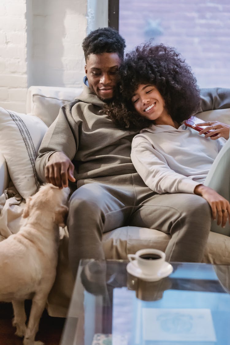 Young Loving Couple Embracing On Sofa And Petting Dog